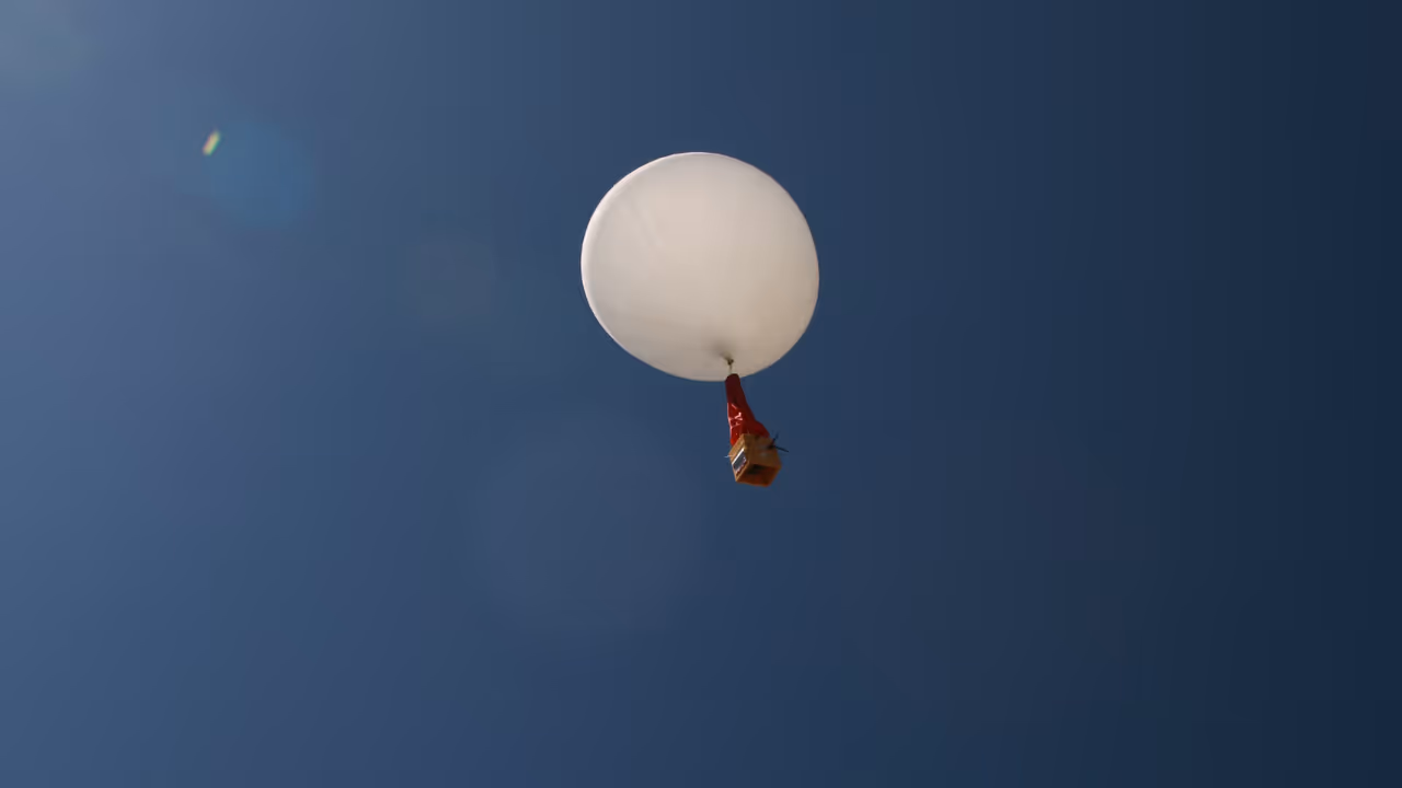 High-altitude weather balloon with attached equipment ascending into clear blue sky.